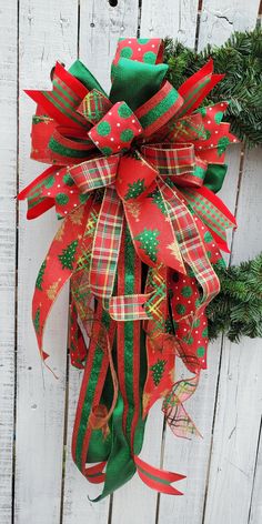 a christmas wreath hanging on the side of a white fence with red and green ribbons