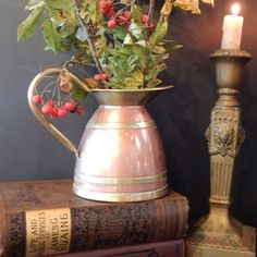 a vase filled with berries and greenery next to a candle on top of an old book