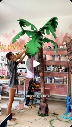 a woman standing next to a palm tree in a room with pink paint on the walls