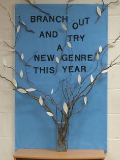 a branch with white leaves in a glass vase on a shelf next to a blue sign that says branch out and try a new gene this year