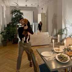 a man holding a dog while standing in front of a dining room table