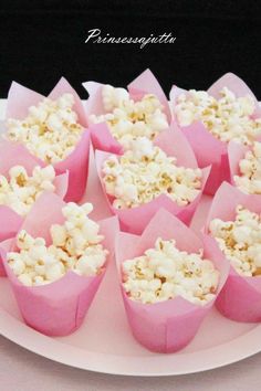 some pink cups filled with popcorn on top of a white plate