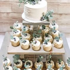 cupcakes are arranged on top of a tiered cake stand with greenery