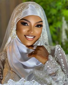 a woman wearing a white veil and headpiece smiles at the camera with her hand on her chin