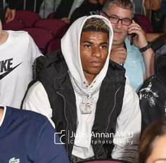 a man in a hoodie sitting next to other people at a sporting event,