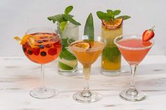 four different types of cocktails are lined up on a white table with green leaves