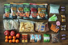 an assortment of snacks laid out on top of a wooden table next to oranges and apples