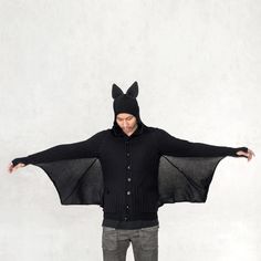 a man wearing a bat costume standing in front of a white wall with his arms outstretched