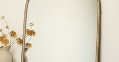 a vase with dried flowers in front of a large gold framed mirror on a white wall