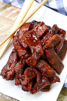 a white plate topped with meat next to chopsticks