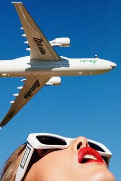 a woman wearing sunglasses looking up at an airplane flying over her head with the words virgin airlines on it's side