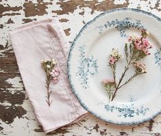 a plate with flowers on it next to a pink napkin and flower potted plant