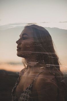 a woman with long hair standing in front of the sun and looking into the distance