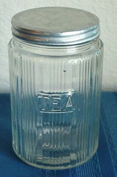 a glass jar with a metal lid sitting on a blue cloth covered tablecloth next to a white wall