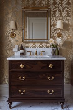 a bathroom vanity with two drawers and a mirror on the wall above it, in front of a gold damask wallpaper