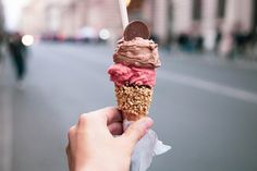 a person holding an ice cream cone with chocolate and candy on top in front of a city street