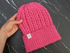 a hand holding a pink knitted beanie on top of a marble countertop