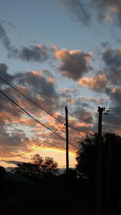 the sun is setting behind power lines and telephone poles, with trees in the foreground