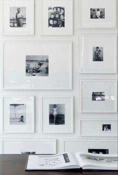 an open book sitting on top of a wooden table in front of a wall filled with pictures