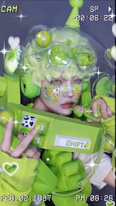 a woman with green hair and goggles holding a video game controller in front of her face