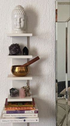 a white shelf filled with books next to a mirror and a statue on top of it