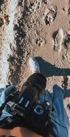 a person is taking a photo in the sand with a camera and some footprints on the ground