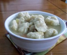 a white bowl filled with dumplings sitting on top of a wooden table next to a napkin