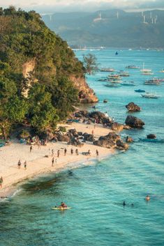 many people are on the beach and in the water near some boats that are out in the ocean