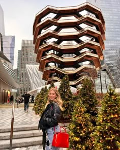 a woman is standing in front of a building with stairs and trees on the sidewalk