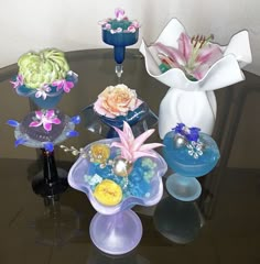 several vases with flowers are sitting on a glass table, and one is filled with water