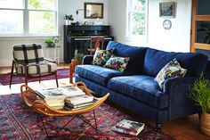 a living room with blue couches and rugs on the wooden floor, windows, and piano in the background