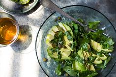 a glass bowl filled with green vegetables next to two glasses