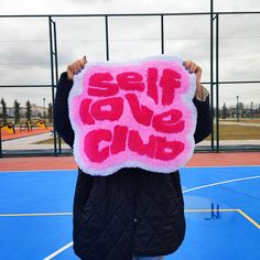 a person holding up a sign with the words self love club written in pink on it