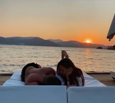 a man and woman laying on top of a white couch in front of the ocean