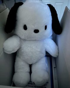 a white stuffed dog with black ears sitting in a box