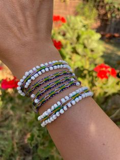 a woman's arm with several bracelets on it and flowers in the background