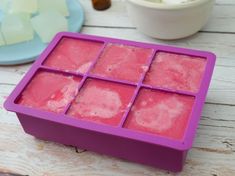 a pink ice tray sitting on top of a wooden table next to a white bowl