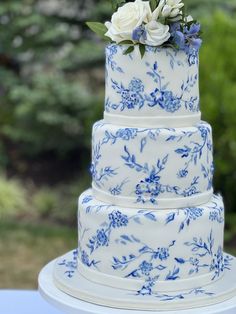 a blue and white three tiered cake with flowers on the top is sitting on a table outside