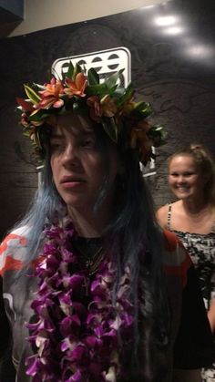 a woman with blue hair wearing a flower crown on her head and another woman in the background