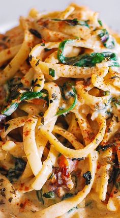 a pasta dish with spinach and cheese on a white plate, ready to be eaten