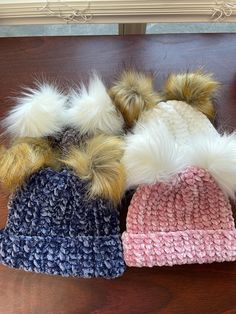 three knitted hats with pom - poms on top of a wooden table