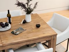 a wooden table topped with white chairs next to a vase filled with fruit