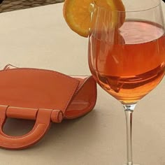 a glass of wine next to an orange slice on a table with a leather case