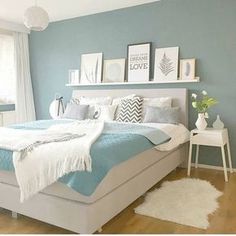 a white and blue bedroom with pictures on the wall above the bed, along with rugs