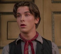 the young man is wearing a vest and red tie with his eyes wide open while standing in front of a door