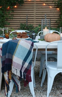 the table is set for dinner outside with candles on it and plaid blanket draped over it