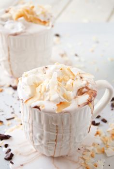 two cups filled with whipped cream on top of a white tablecloth covered in chocolate shavings