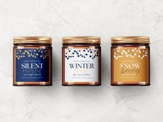 three jars of winter candles on a white surface with gold and blue decorations around them