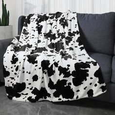 a black and white cow print blanket sitting on top of a couch next to a potted plant