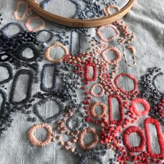 a close up of a table cloth with beads on it and a wooden hoop in the background